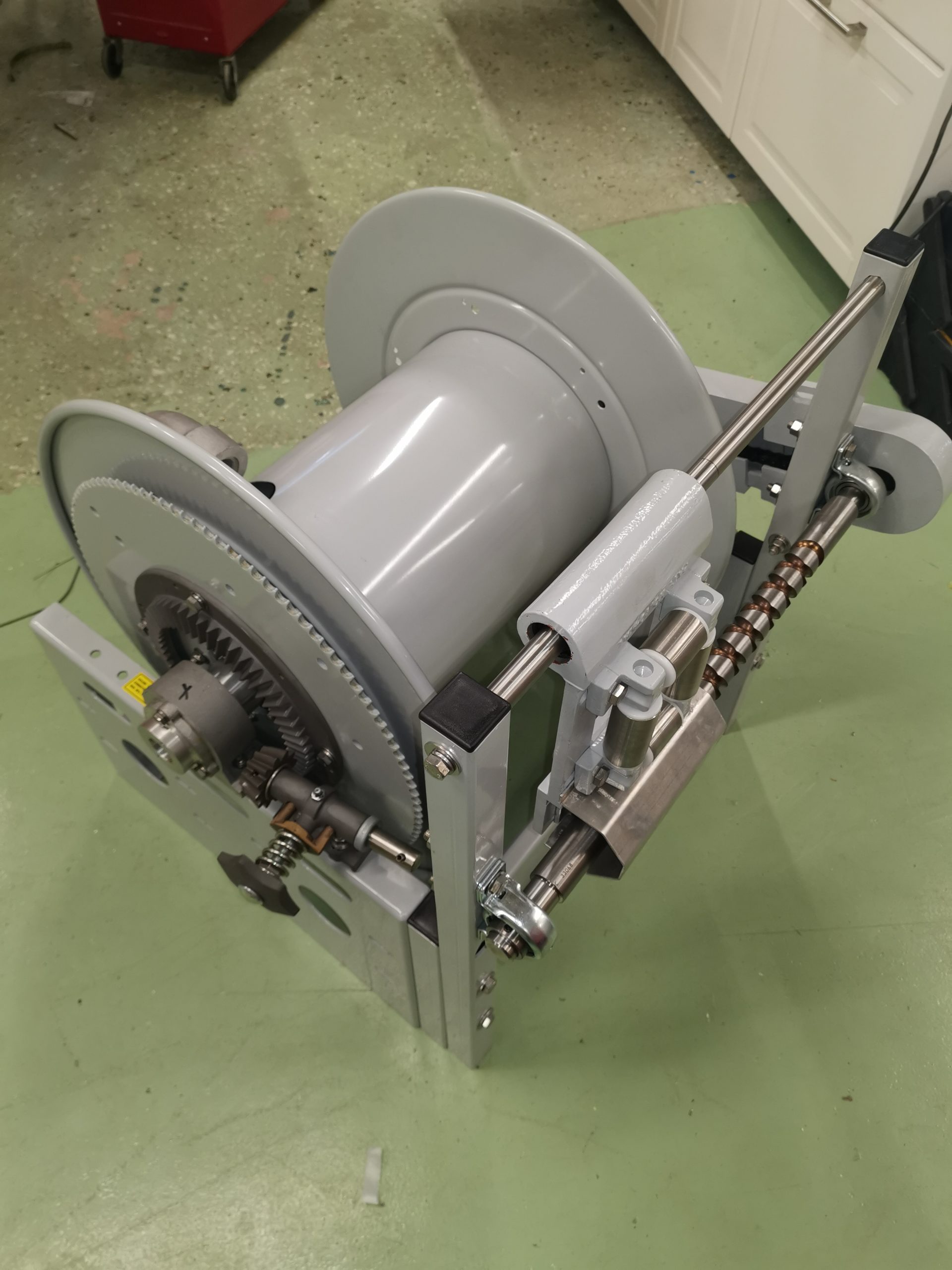 En Slangvinda modell För 50m Ø2" slang- Motordriven 24VDC rulle står på ett bord i ett rum.